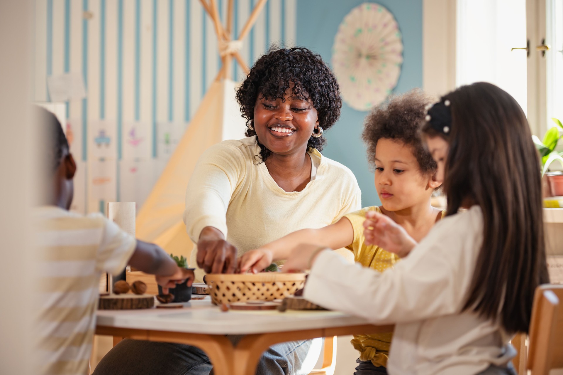 Preschool teacher guides a diverse group of children in a natural materials activity in a bright, creative classroom setting focused on hands-on learning.