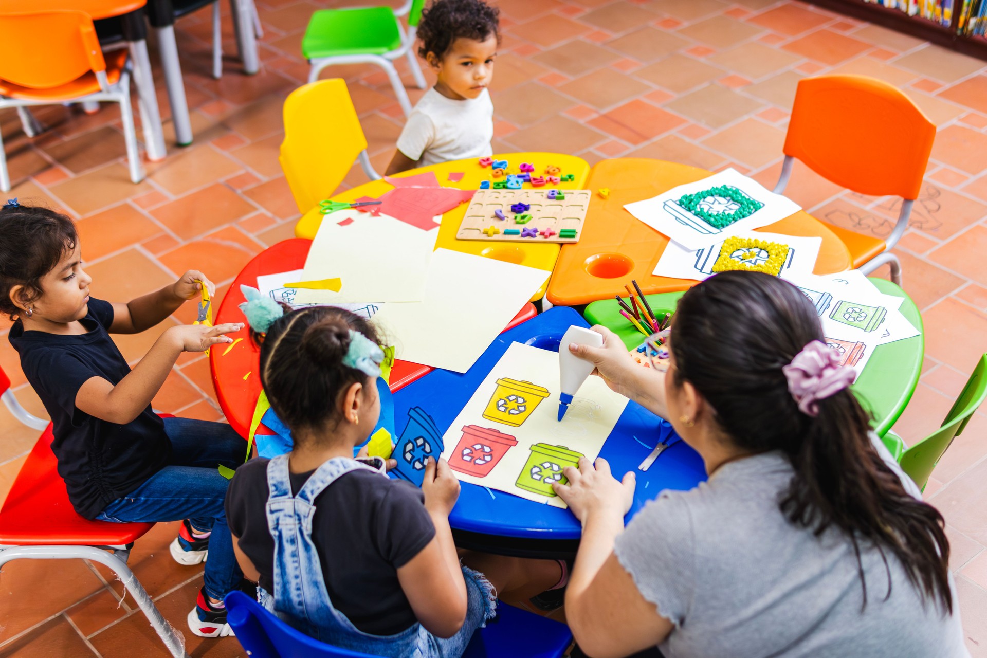 Teacher helping preschool children with arts and crafts activity about recycling